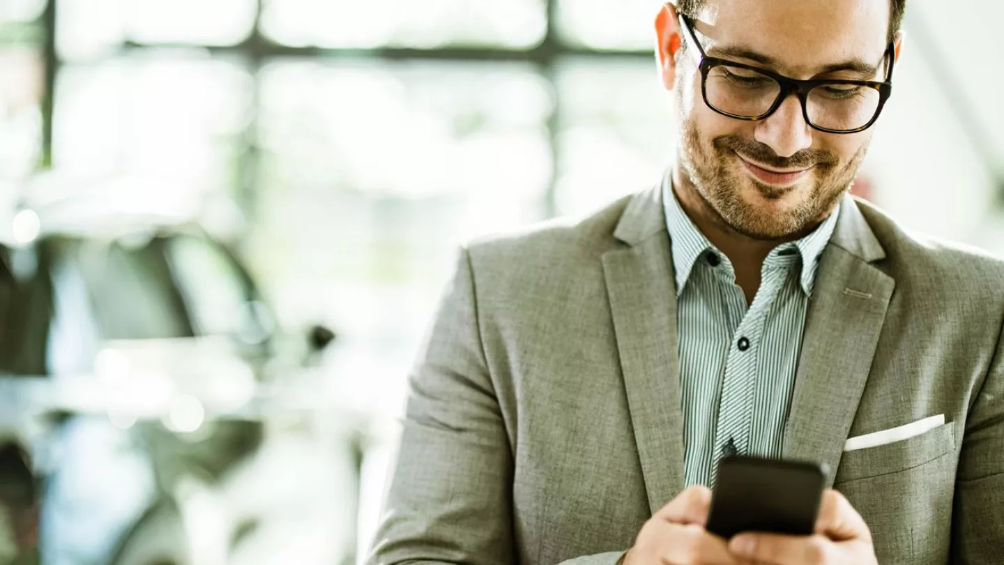 Man looking at his phone while shopping for a car