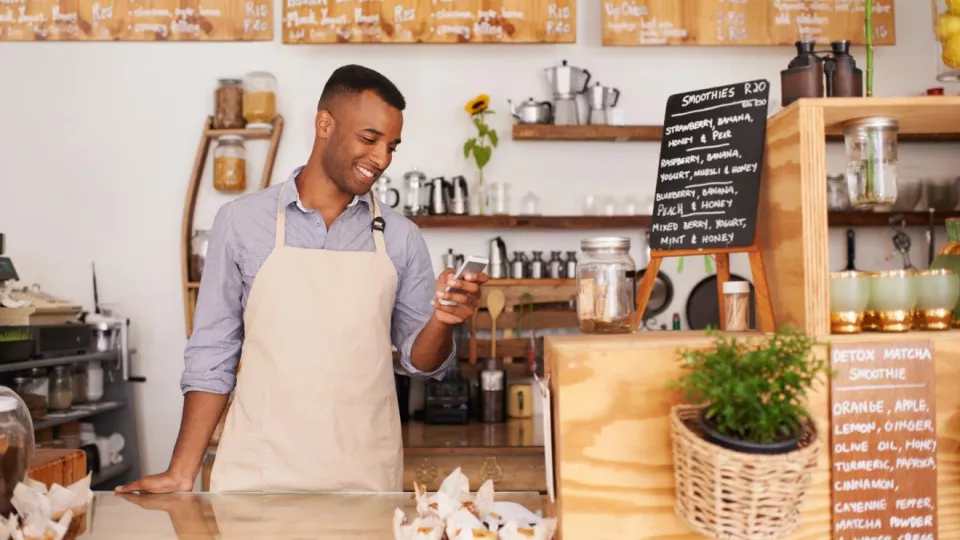 A man at a cafe checks his phone while working